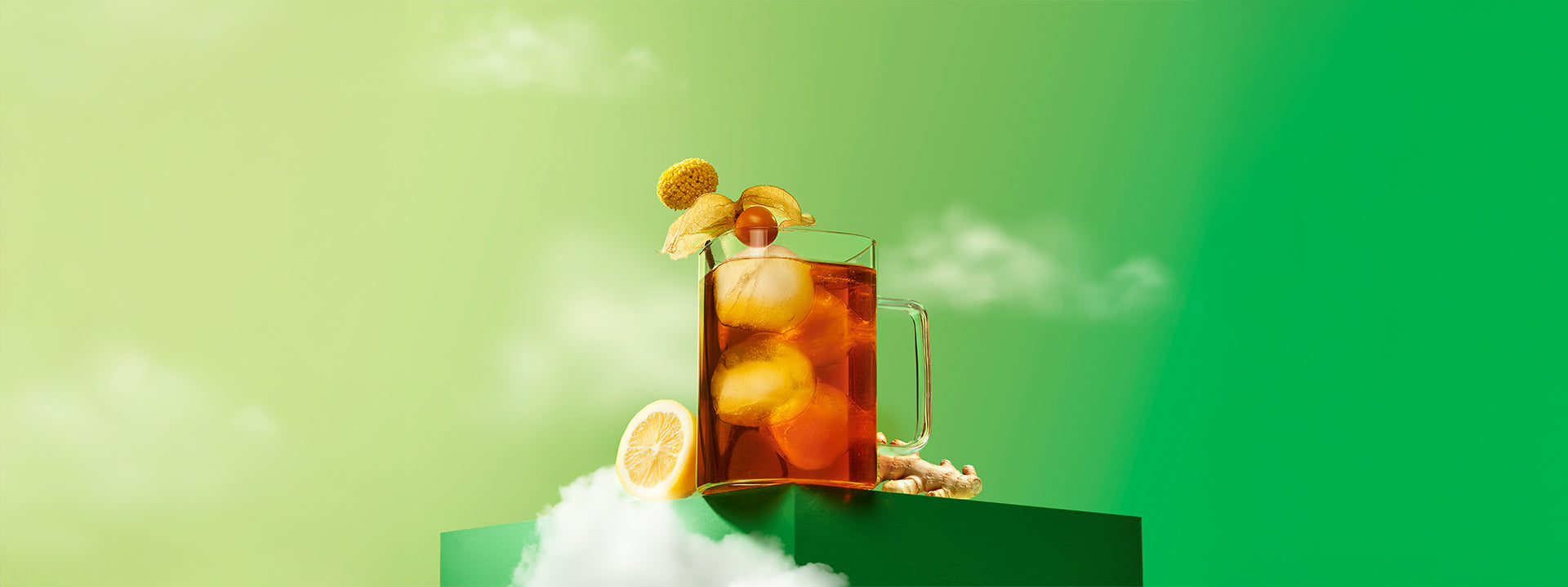 Une tasse en verre transparent contenant du thé coloré avec une cerise de terre sur le rebord, sur un arrière-plan vert avec des nuages.
