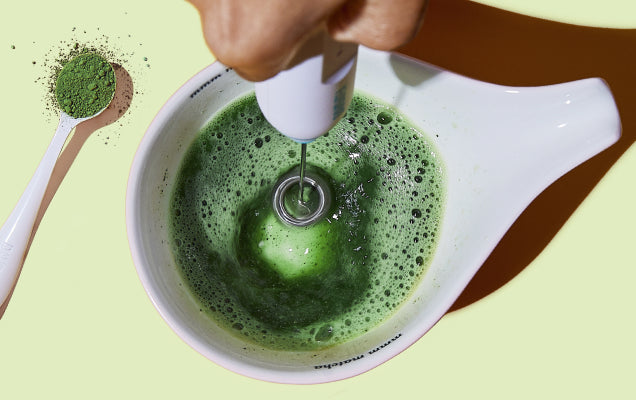 Whisking matcha in a green bowl with a bamboo whisk