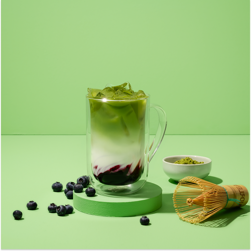 blueberry matcha  iced latte surrounded by matcha tools and berries