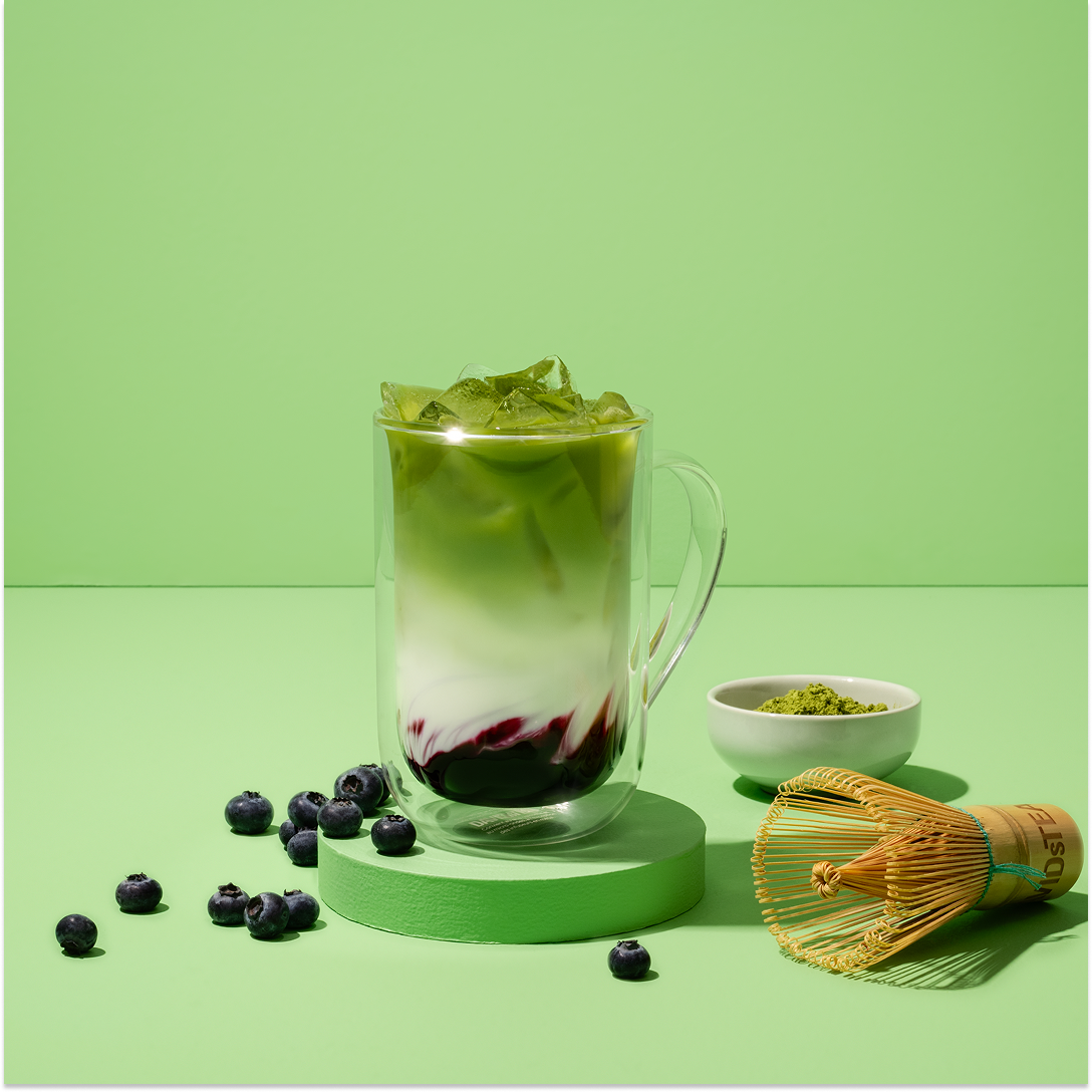 blueberry matcha  iced latte surrounded by matcha tools and berries