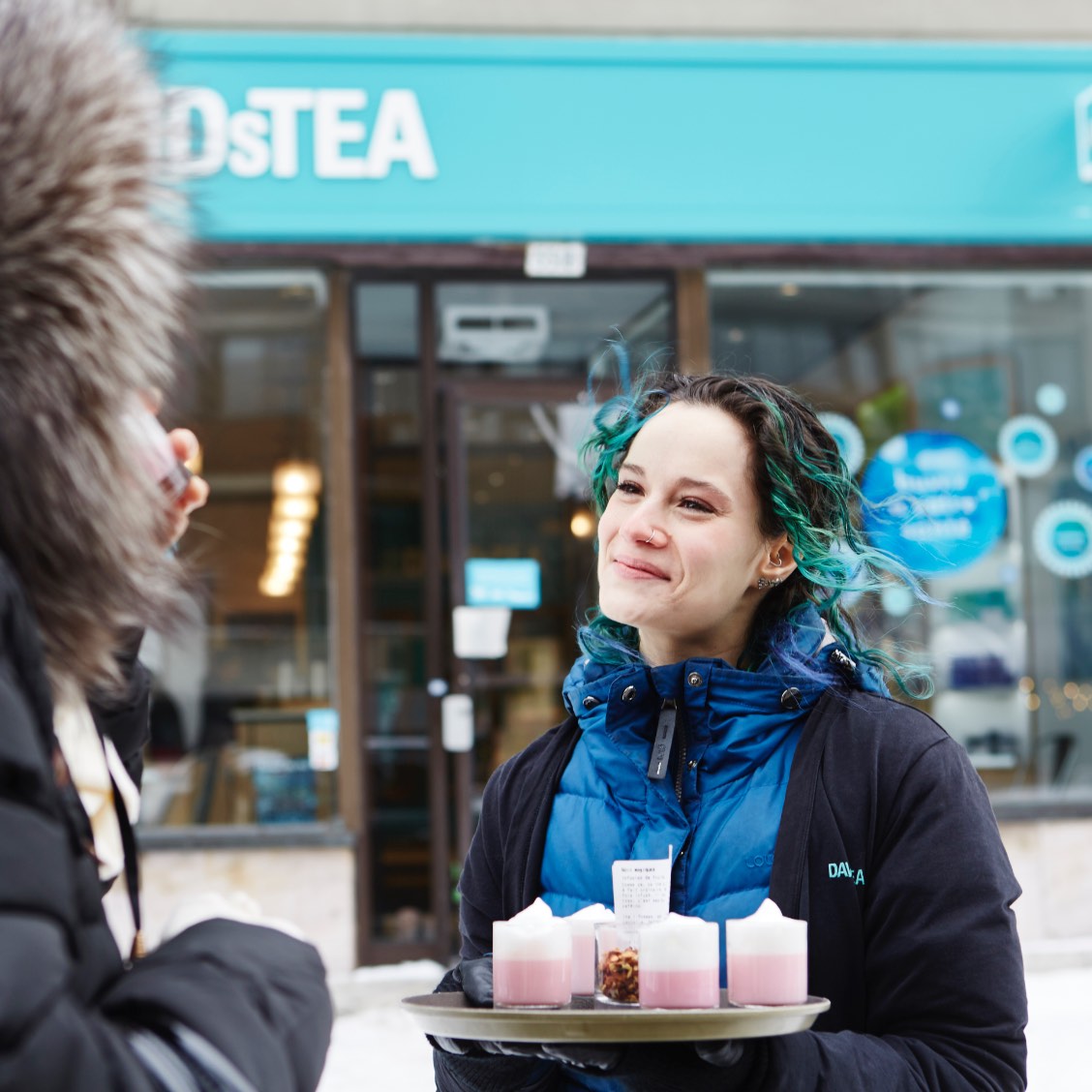 Person in a DAVIDsTEA apron holding a cup of tea outside a store